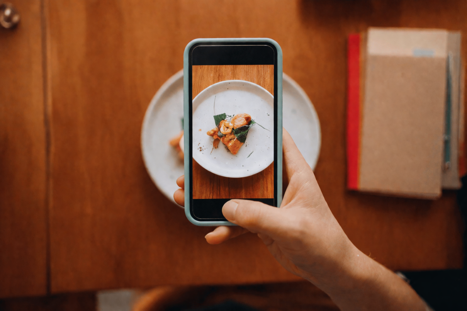 Main tenant un smartphone photographiant une assiette dressée sur table en bois, composition culinaire minimaliste vue du dessus
