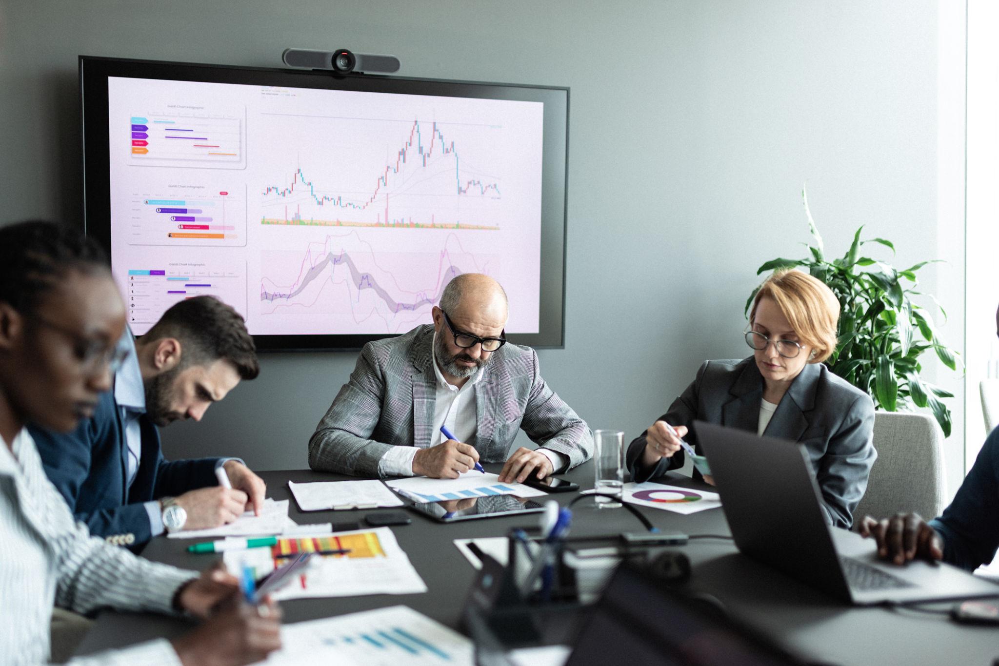 Équipe en réunion analysant des graphiques et données de marché sur un écran, illustrant une étude stratégique et une prise de décision basée sur les performances et tendances