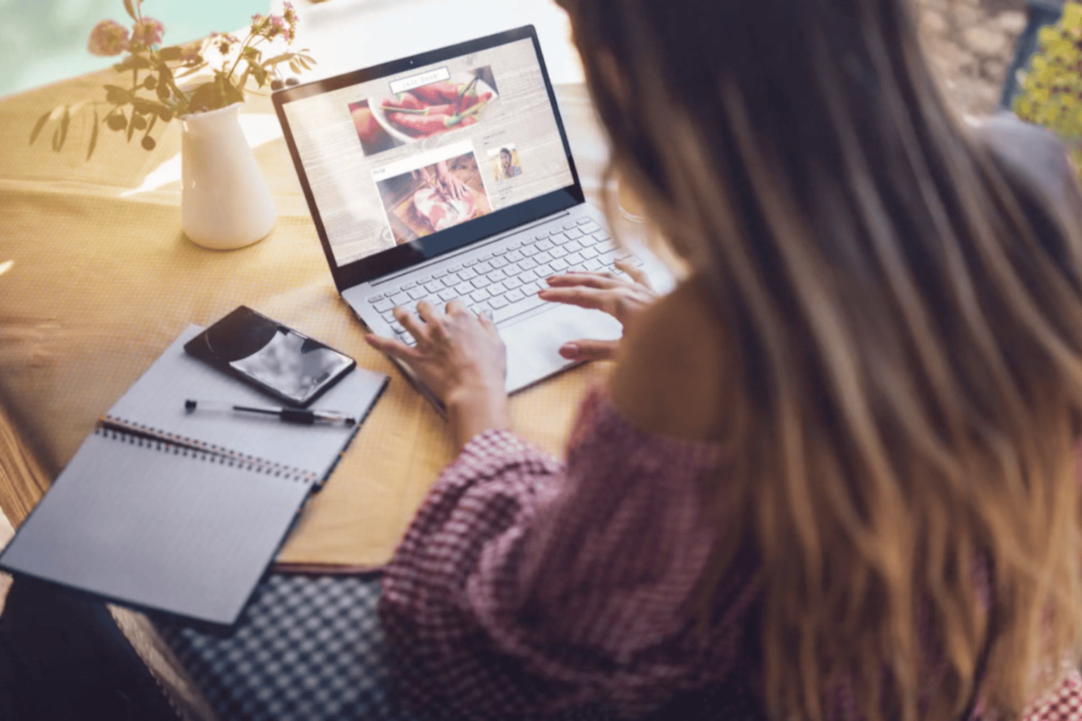 Femme travaillant sur ordinateur portable à domicile, consultant un site web avec smartphone et carnet sur la table