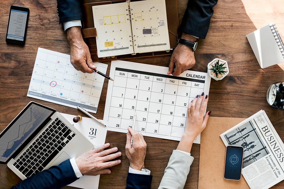 Équipe organisant un calendrier de contenu sur table avec agendas, ordinateur et documents, illustrant la planification éditoriale et la gestion stratégique des publications