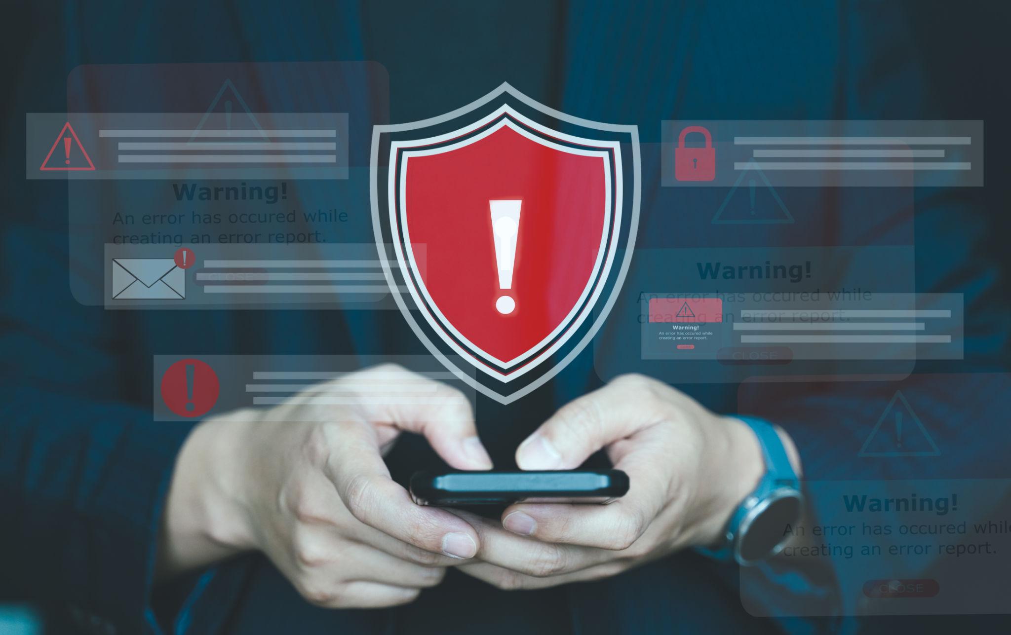 Personne utilisant un smartphone avec un bouclier de sécurité et des alertes en arrière-plan, illustrant la surveillance et la détection de menaces informatiques