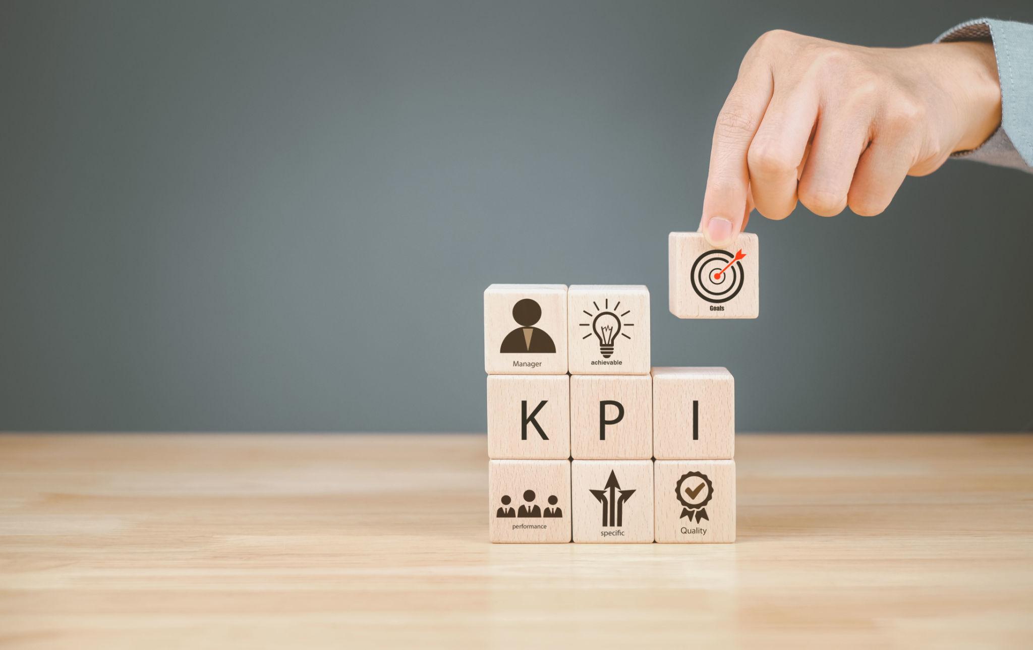 Main plaçant un bloc avec une cible au-dessus de cubes “KPI”, illustrant le suivi des indicateurs de performance et l’atteinte des objectifs